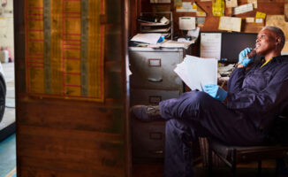 Auto repair shop owner reviewing paperwork and discussing business insurance coverage gaps by phone
